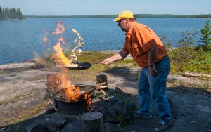 A guide cooks a pan of mushrooms over the bonfire on shore