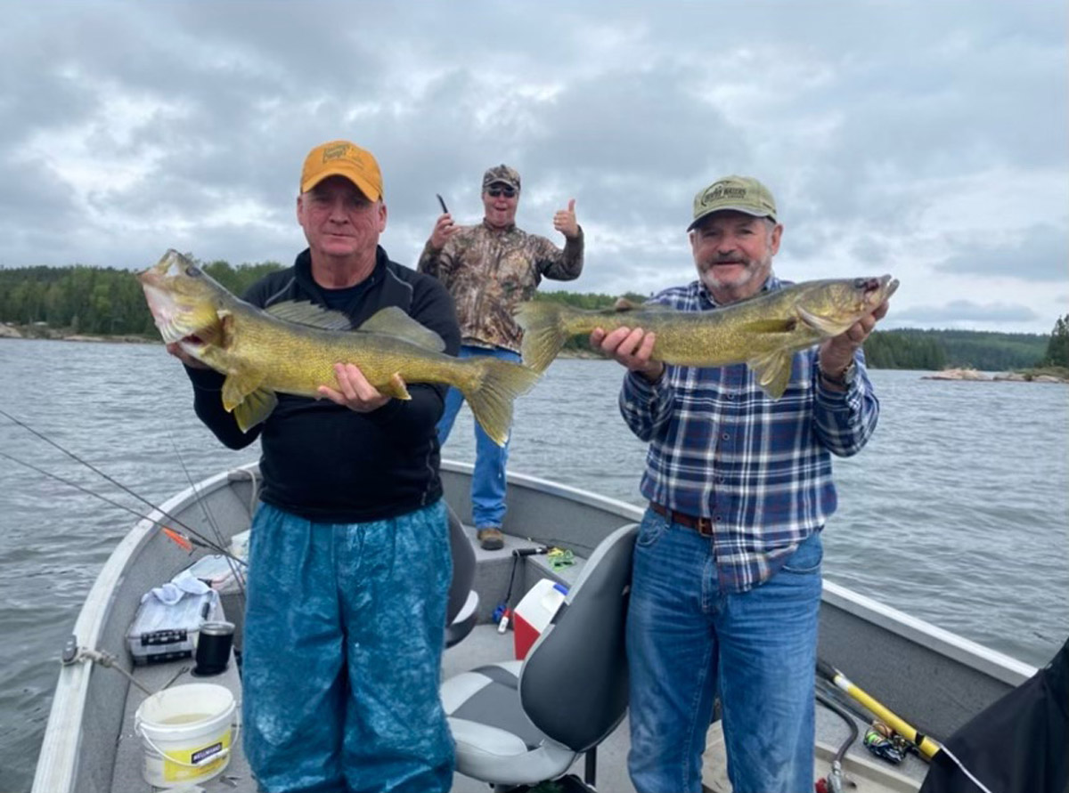 Two fishermen holding up trophy walleye in the boat.