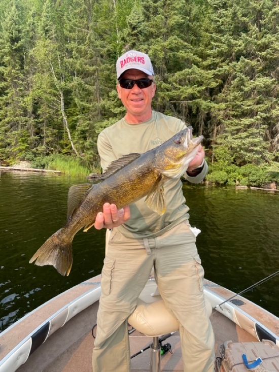 Man holding his big walleye he caught standing in a boat that is near shore