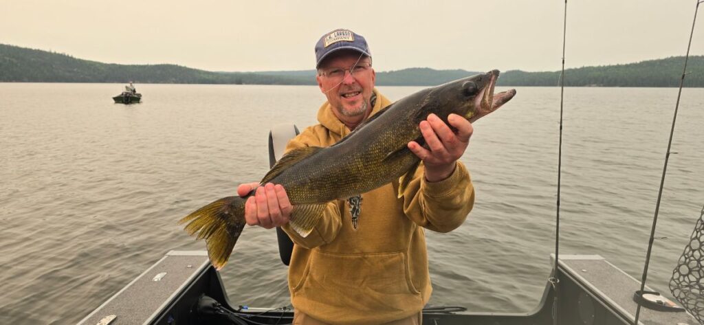 Man holding up a large walleye in a boat with smoky skies at Halley's Camps