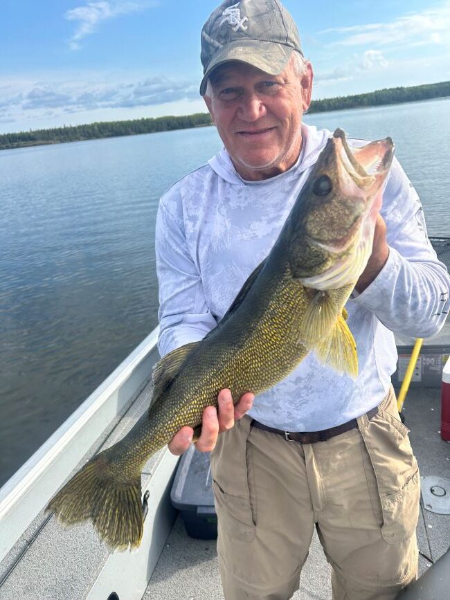 man holding a fish on a sunny day while fishing at Halley's Camps