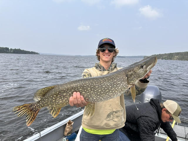 Young man holding a fish with a large northern pike holding it in a boat on a sunny day!