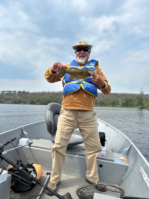 Man holding a fish in the front of a fishing boat on a lake