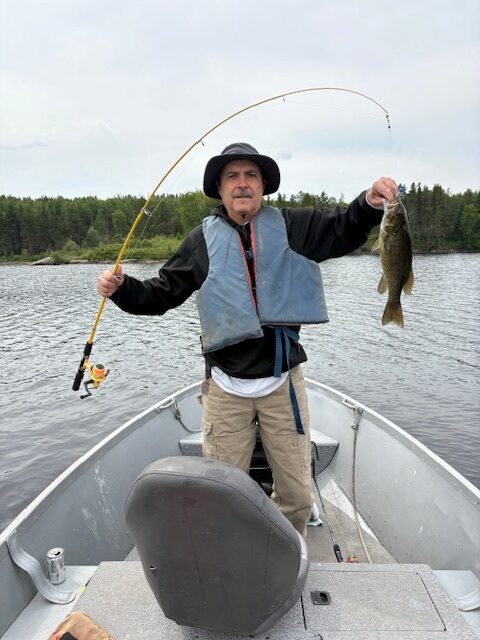 Man holding a bass with his rod bent over with the fish at the other end
