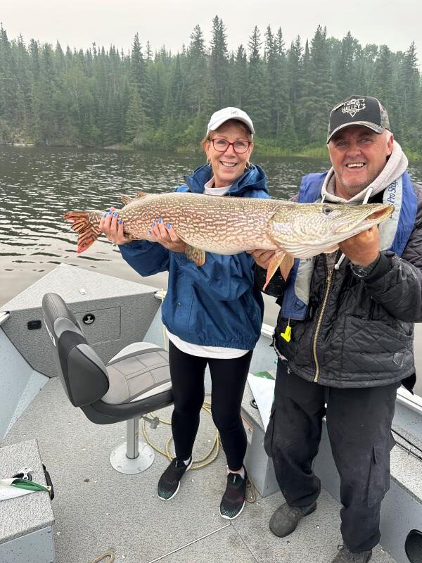 Woman holding up 1/2 the fish and her guide holding the other on a cloudy day while fishing.