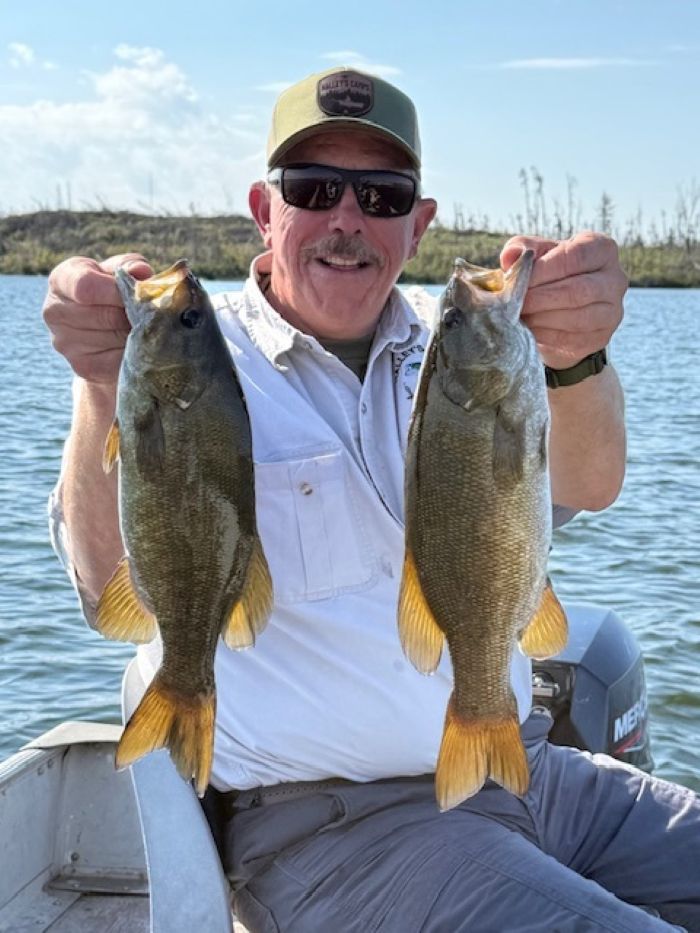 man in boat holding up 2 bass by the lips