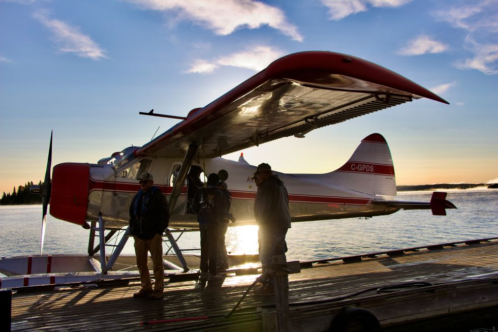 5 men standing on a dock with a float plane with the sun coming up getting ready to board.