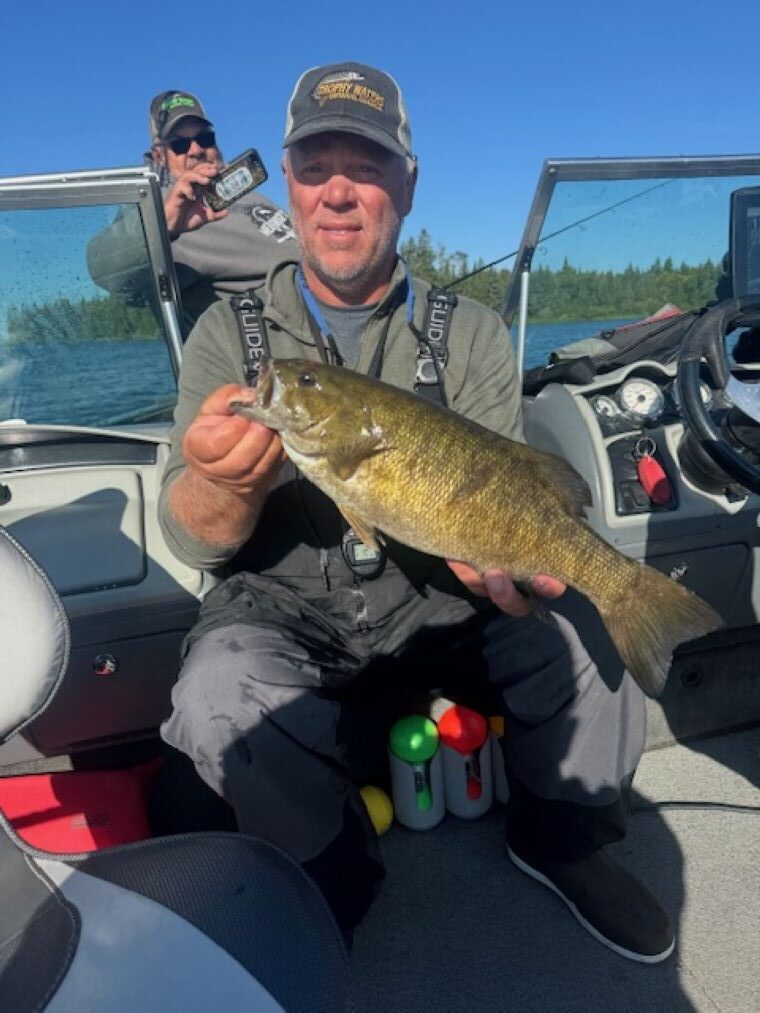 Man holding up a fish while squatting in a boat on a sunny day