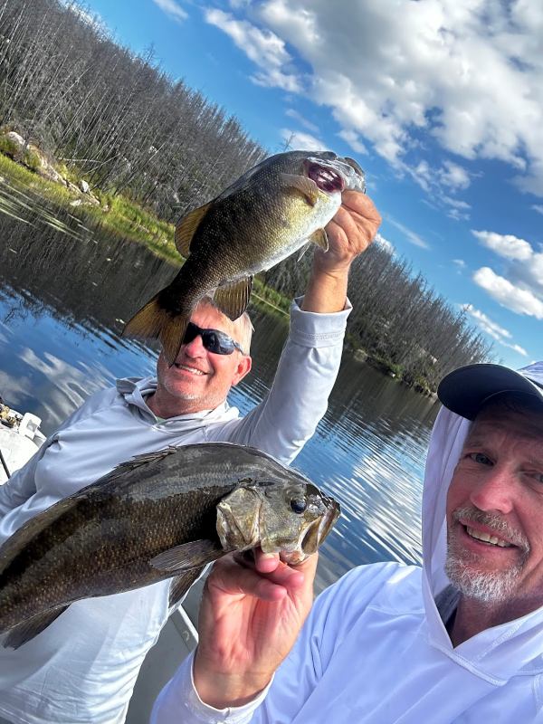 2 men holding up their smallmouth bass catches while fishing on a sunny day with calm waters