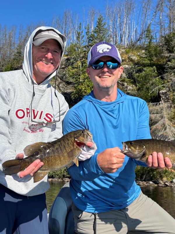 2 men fishing in a boat close to shore each holding a bass