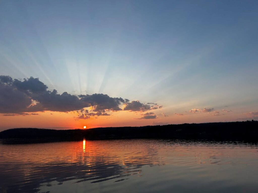 Sunrise at Rex Lake Outpost coming over the tree tops across the flat water lake