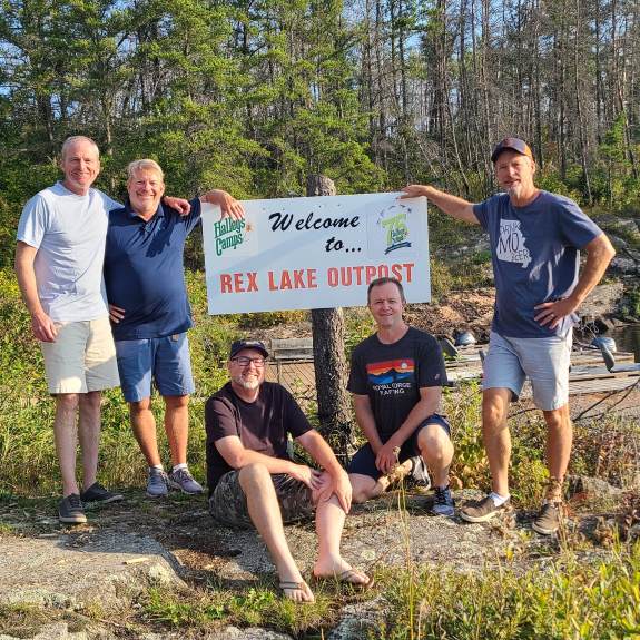 5 men posing in front of the fishing camp, Rex Lake Outpost, sign