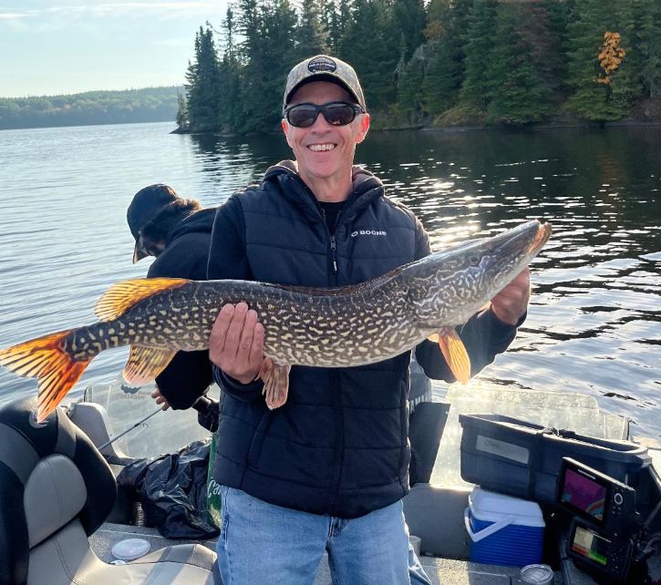 Man holding a northern pike in a Halley's Camps boat fishing in Canada on a sunny day!