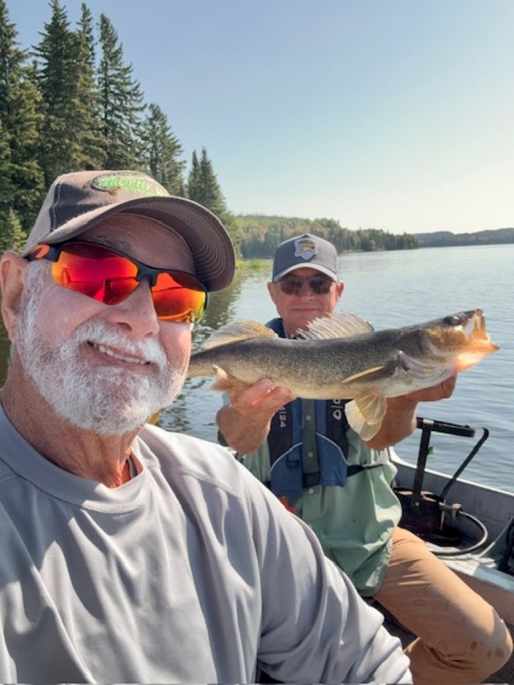 2 men in a boat one holding a fish and the other is taking the selfie with both men in the picture!
