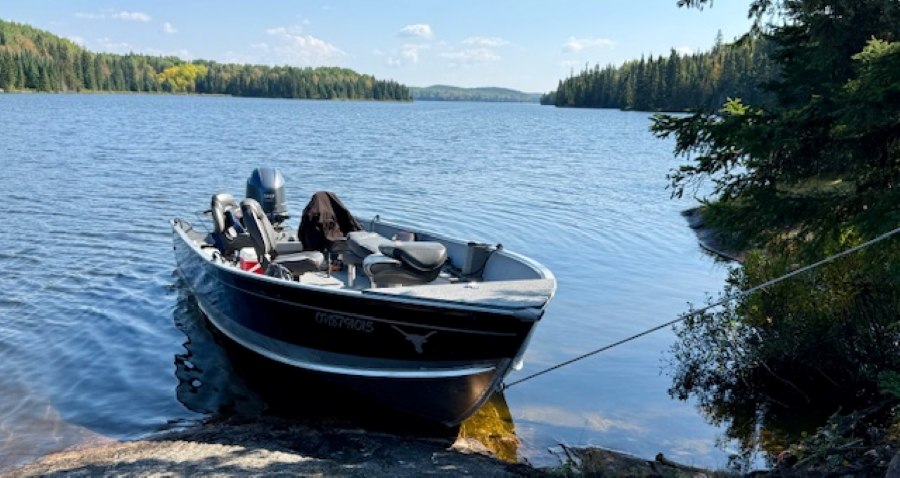 Boat sitting on a lake at the edge of shore where it is tied up as the fishermen are having lunch on shore.