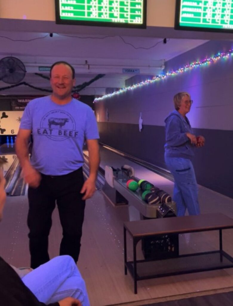 a mother and her adult son both at the bowling alley standing on the bowling lane
