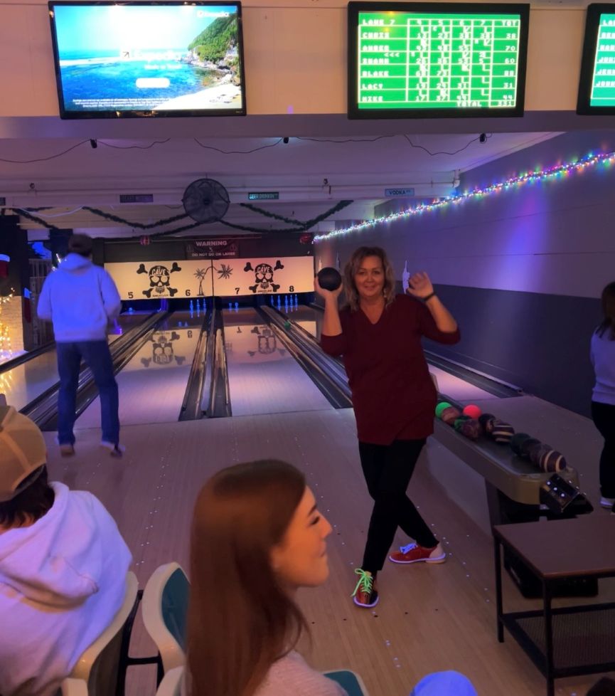 Woman dancing as part of a bowling game holding a bowling ball standing before throwing the ball down the bowling lane