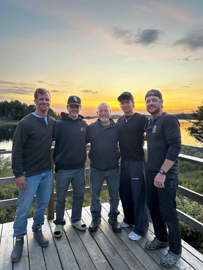 5 family members standing on the cabin deck with the lake and sunset behind them